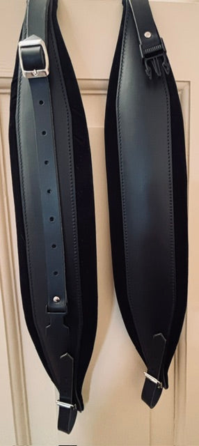 Two black leather accordion straps with metal hardware with built in back strap  on a beige background